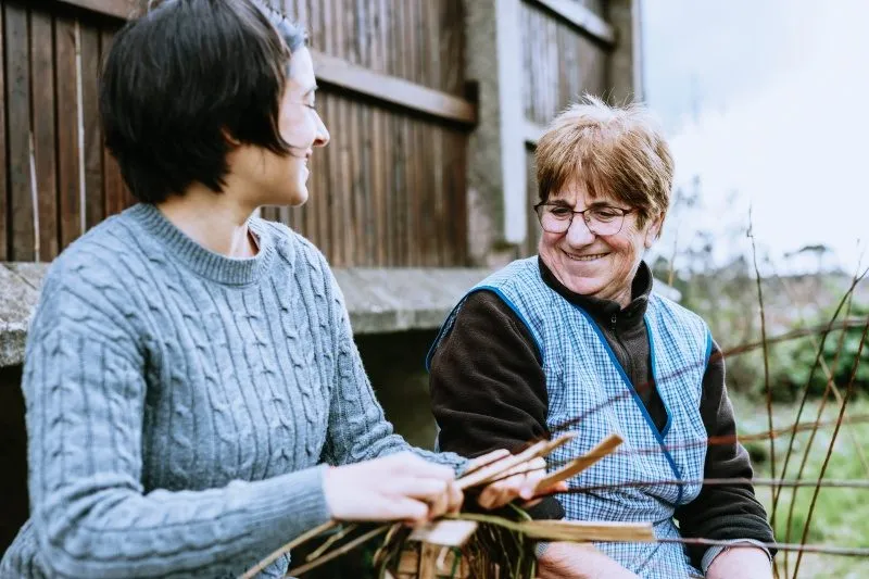 Jüngere und ältere Frau sitzen lachend vor einer Holzhütte