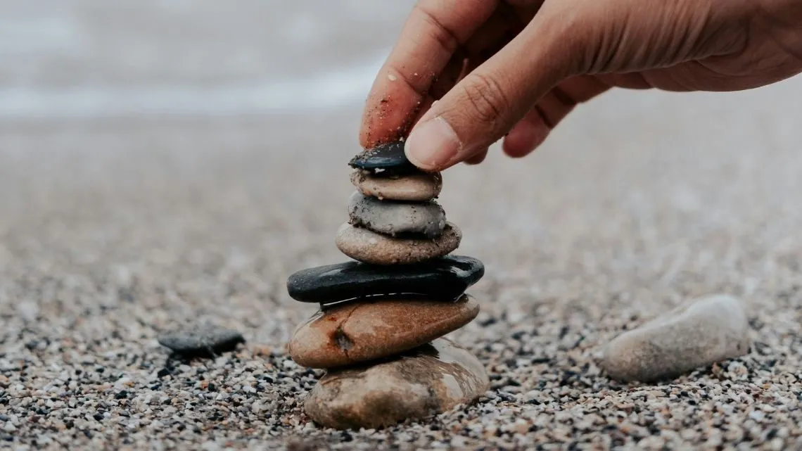Hand stapelt flache Kieselsteine zu einem Türmchen am Strand